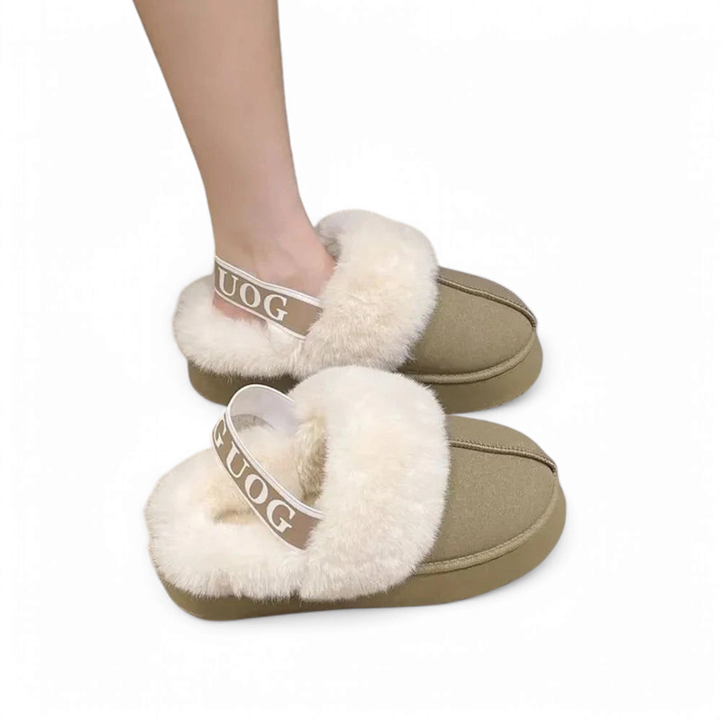 A pair of gray faux suede slippers with fur trim; one being worn by a woman, the other placed next to her foot on the floor.