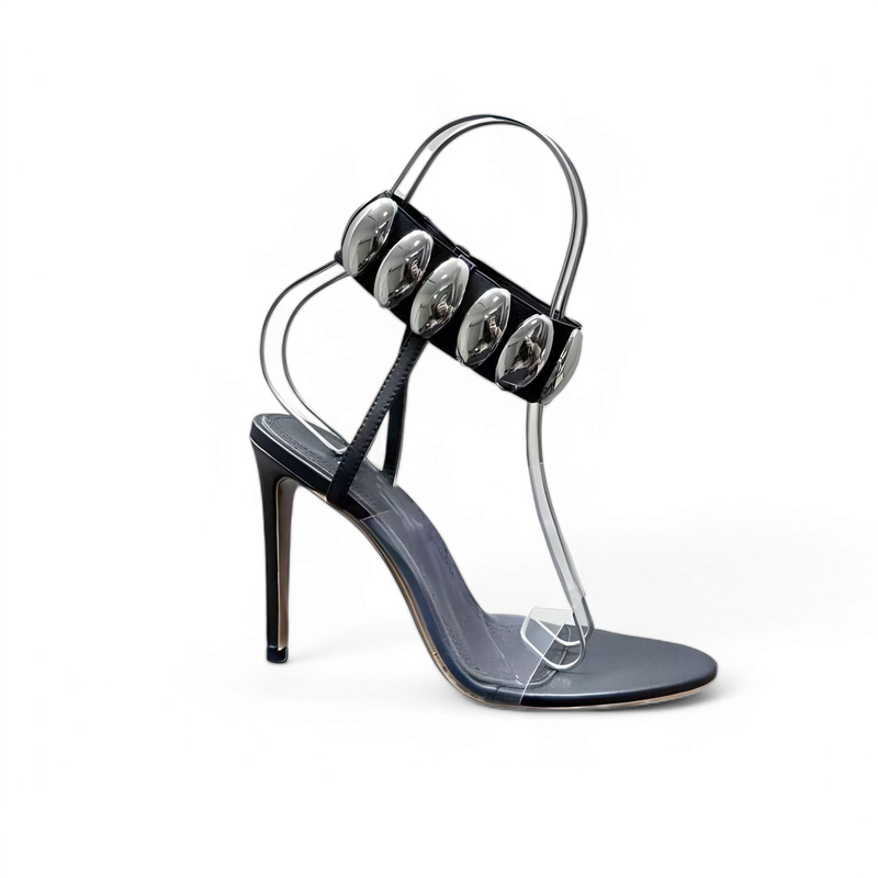 Side view of a black stiletto sandal with clear pvc vamp and silver-oval ankle décor.