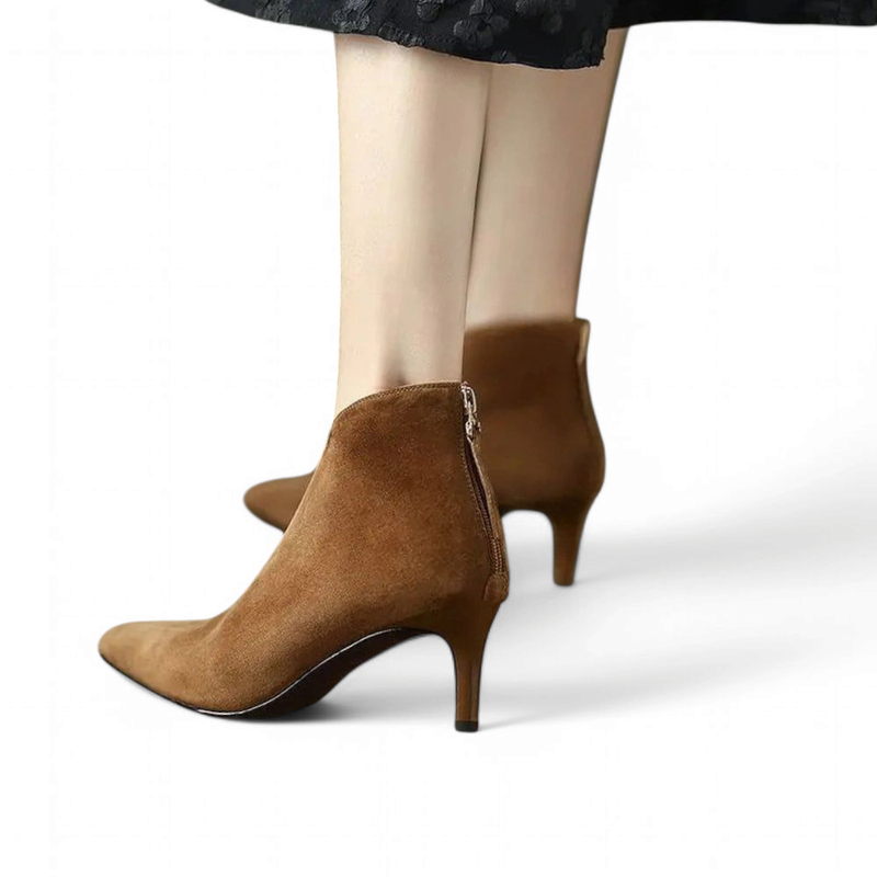 Brown suede boots with slim heel worn on feet, rear-side angle with partly open zipper.
