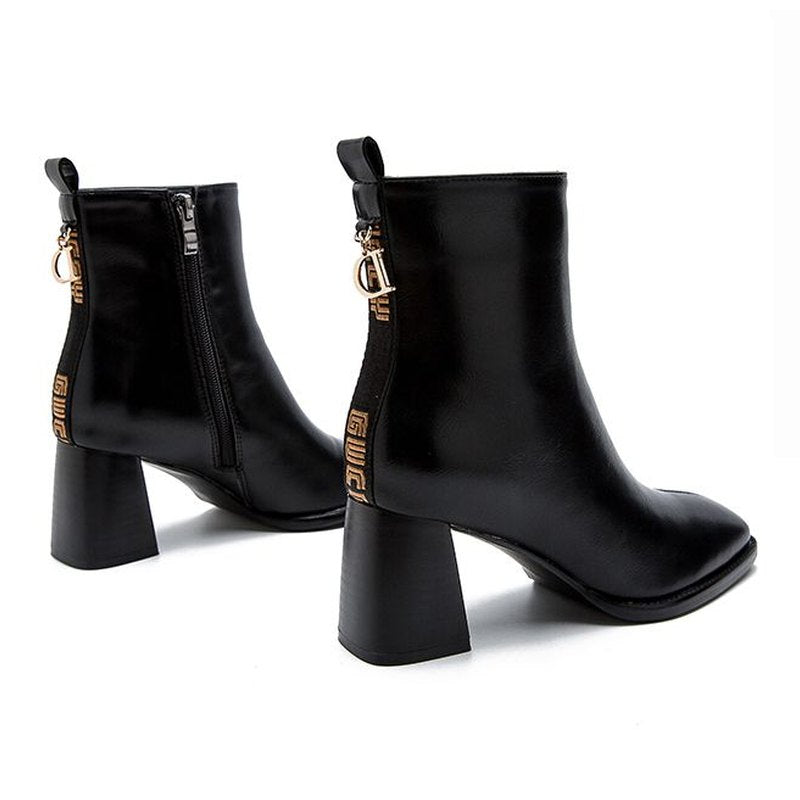 Pair of black boots showing back strap, logo tape, metal ring and zipper.