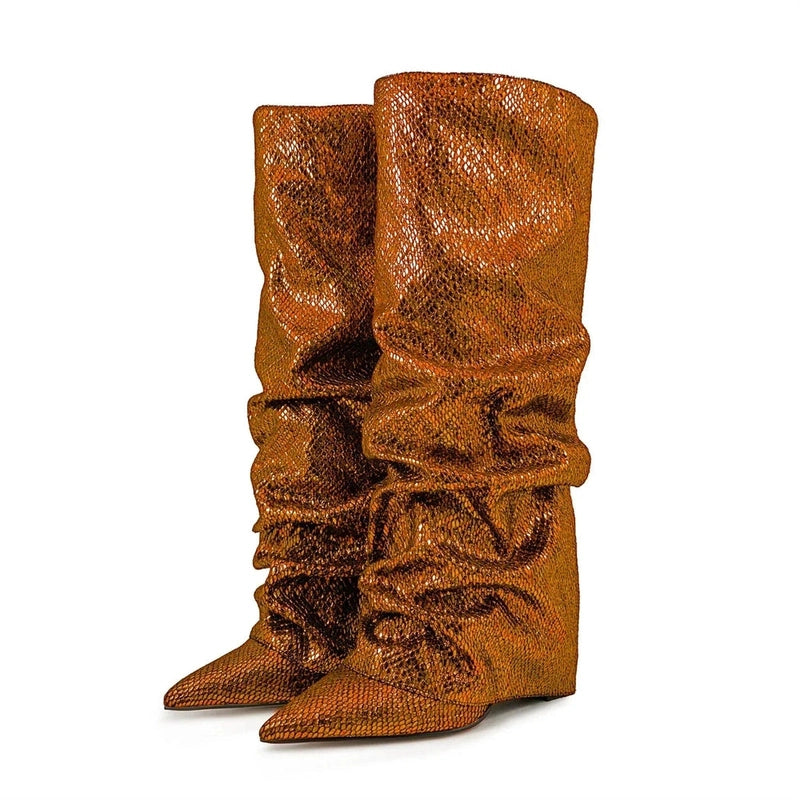 Pair of bronze knee-high boots shown from a front-side angle, featuring a pointed toe, jeweled slouchy shaft, and hidden wedge heels, displayed on a white background.