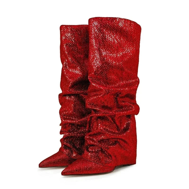 Pair of rose-colored knee-high boots shown from a front-side angle, featuring pointed toes, slouchy jeweled shafts, and concealed wedge heels, placed on a white background.