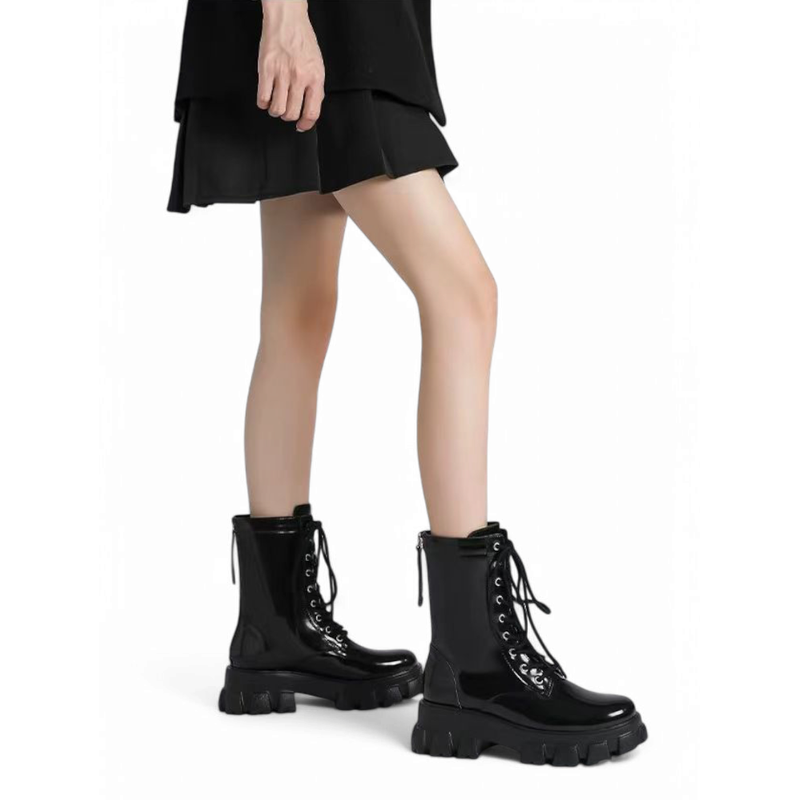 A woman wearing glossy black chunky heel boots while standing.
