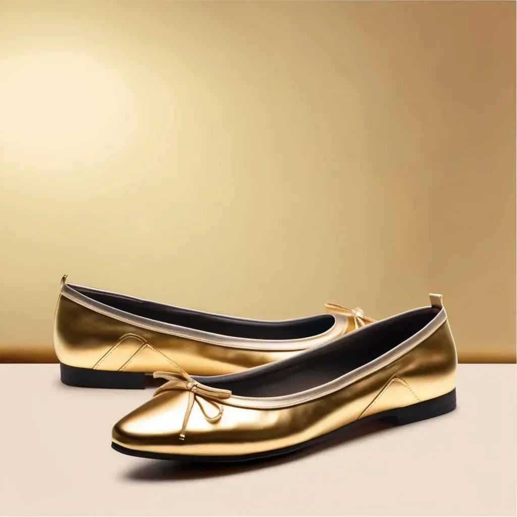 Pair of metallic gold ballet flats with a round toe, small front bow, dark lining, and black outsole on a neutral gold background.