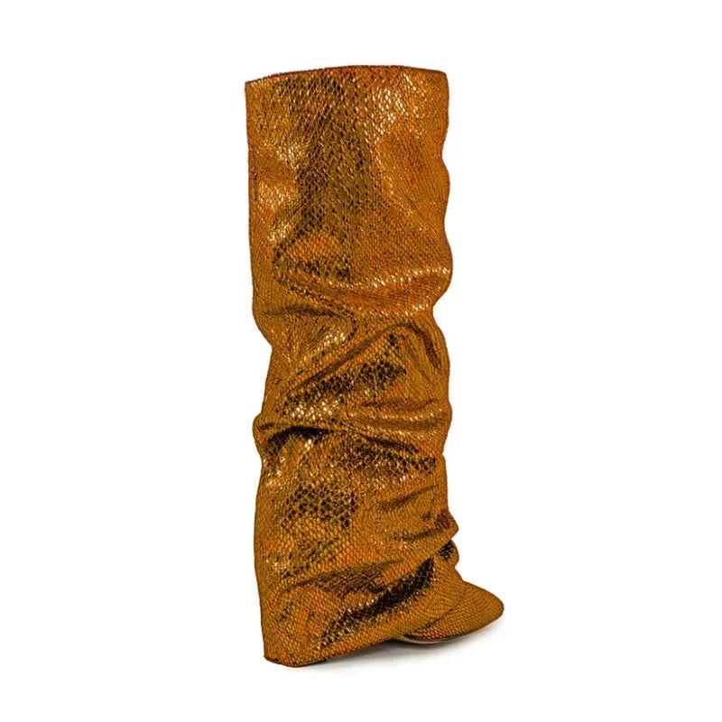 Angled back view of a bronze knee-high boot with a slouchy jeweled shaft, pointed toe, and hidden wedge heel, placed on a white background.