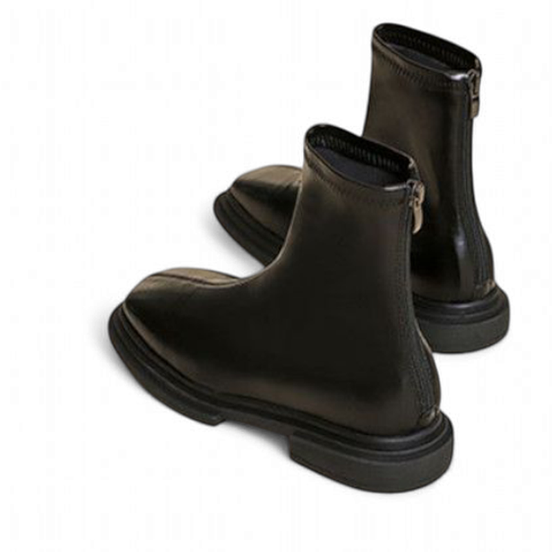 A pair of black leather boots with thick soles and rear zippers, shown from an angled rear view revealing both sides.