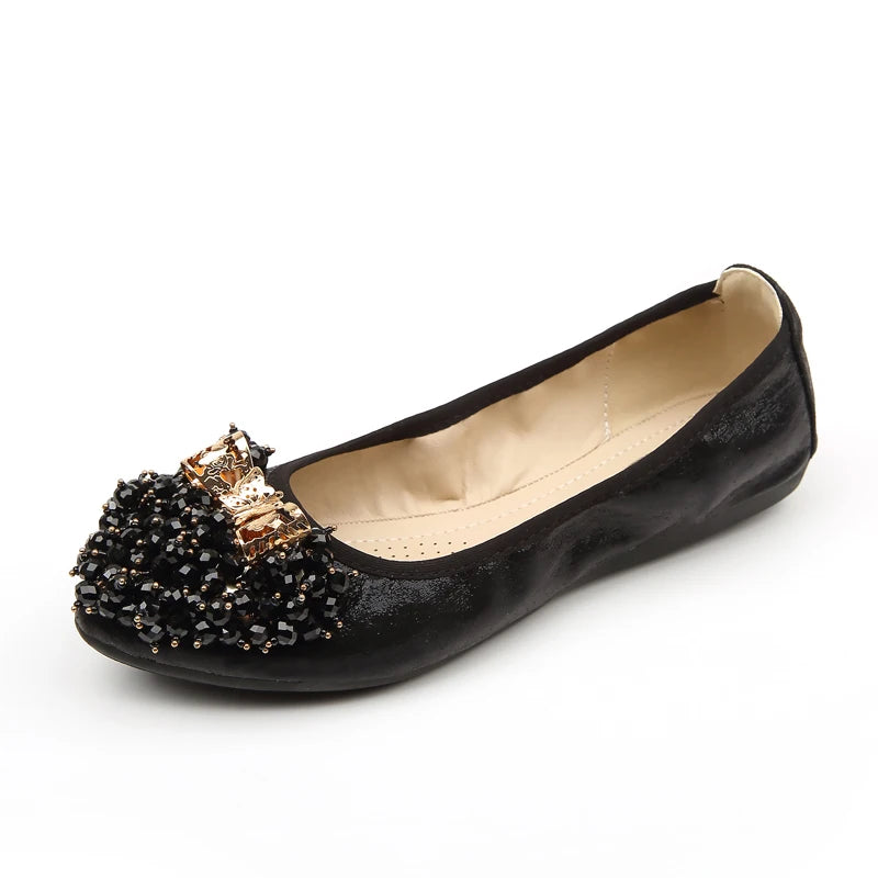 Black foldable ballet flat with clustered black beads and satin-gold bow on the toe, shown from the side.