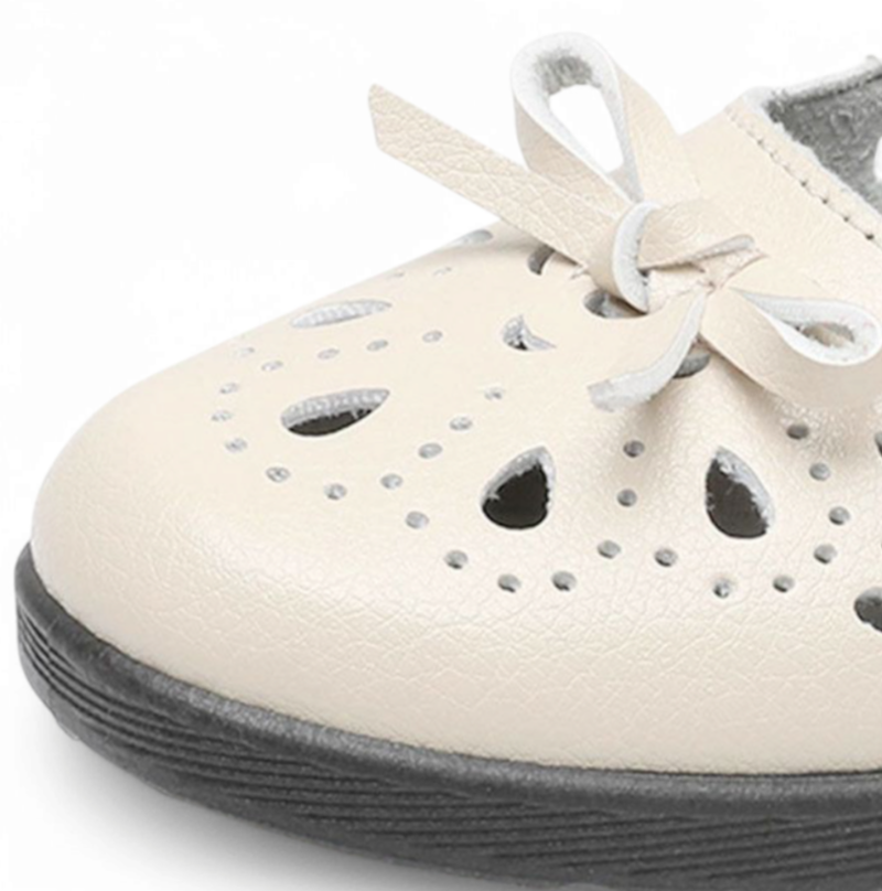 Close-up of beige shoe toe with small bow, decorative perforations, and low black sole.