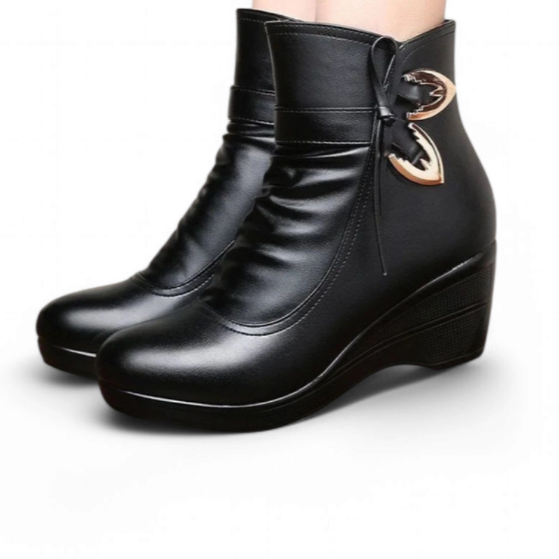 Pair of black leather ankle wedge boots with gold butterfly hardware, shown on feet.