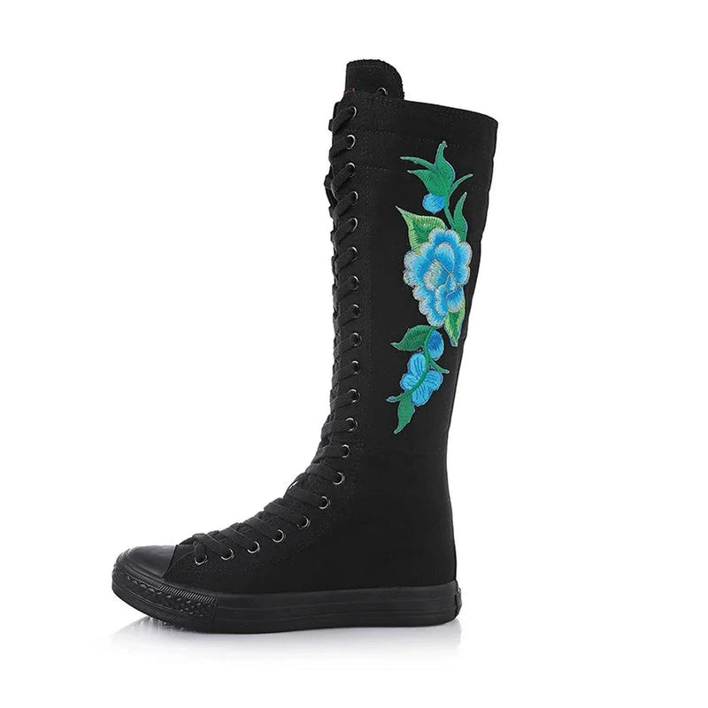 Black knee-high canvas boot with full lacing and blue floral side embroidery.
