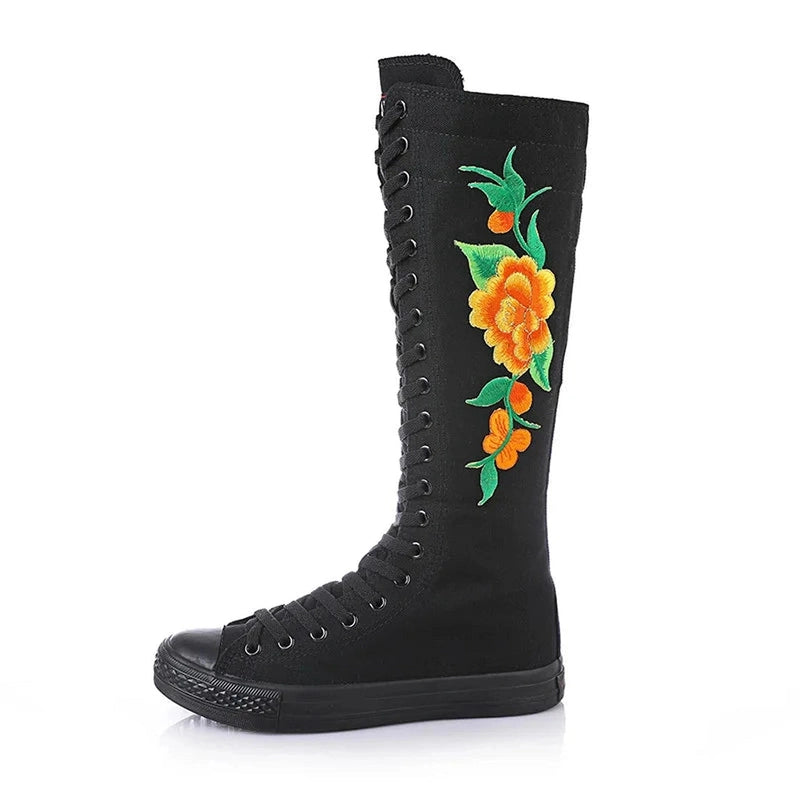 Black knee-high canvas boot showing orange blossom embroidery and green foliage.

