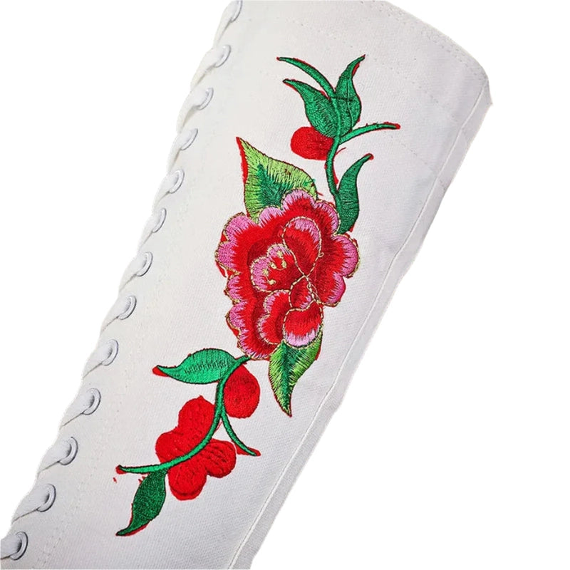 Close-up of red flower and green leaves embroidery on white canvas with eyelets visible.
