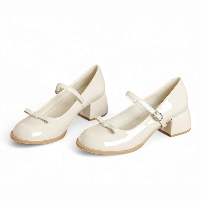 Studio pair of glossy beige Mary-Jane pumps with block heels, gentle side angle on white.
