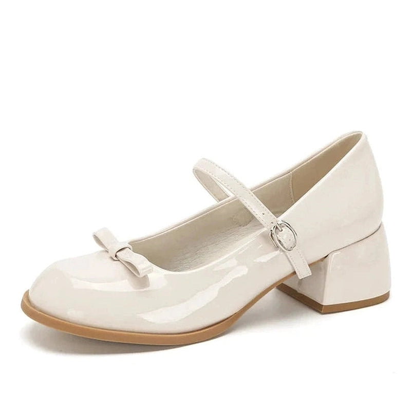 Glossy beige Mary-Jane with mid block heel and bow, side studio view on white background.