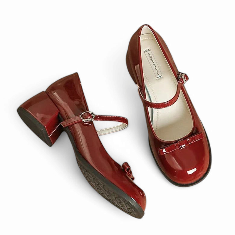 Pair of glossy burgundy Mary-Jane pumps, one tilted showing patterned sole, white backdrop.