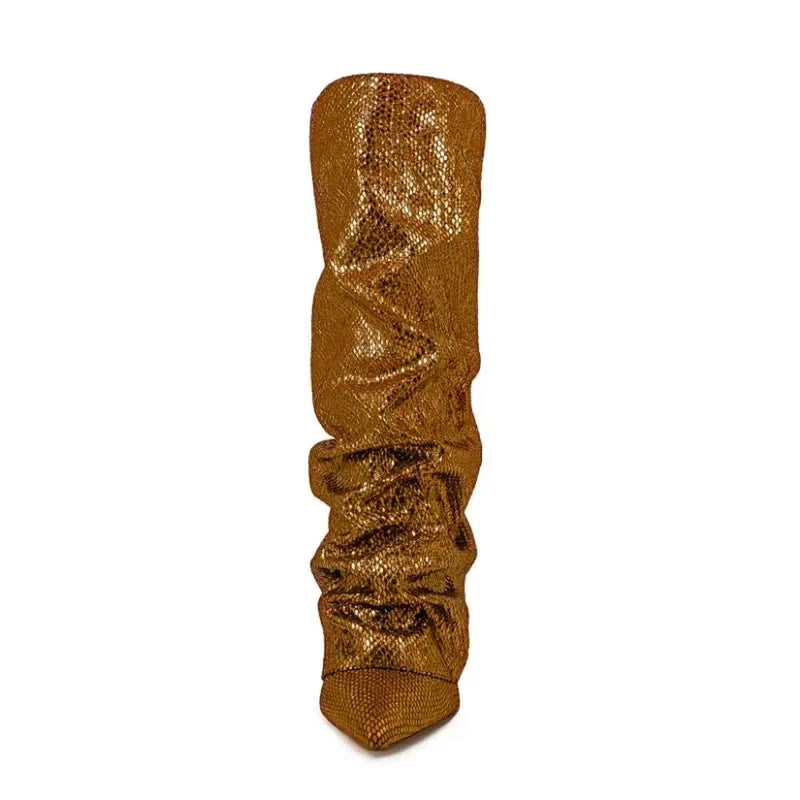 Front view of a bronze knee-high boot with a pointed toe, slouchy jeweled shaft, and shimmering texture, shown against a white background.