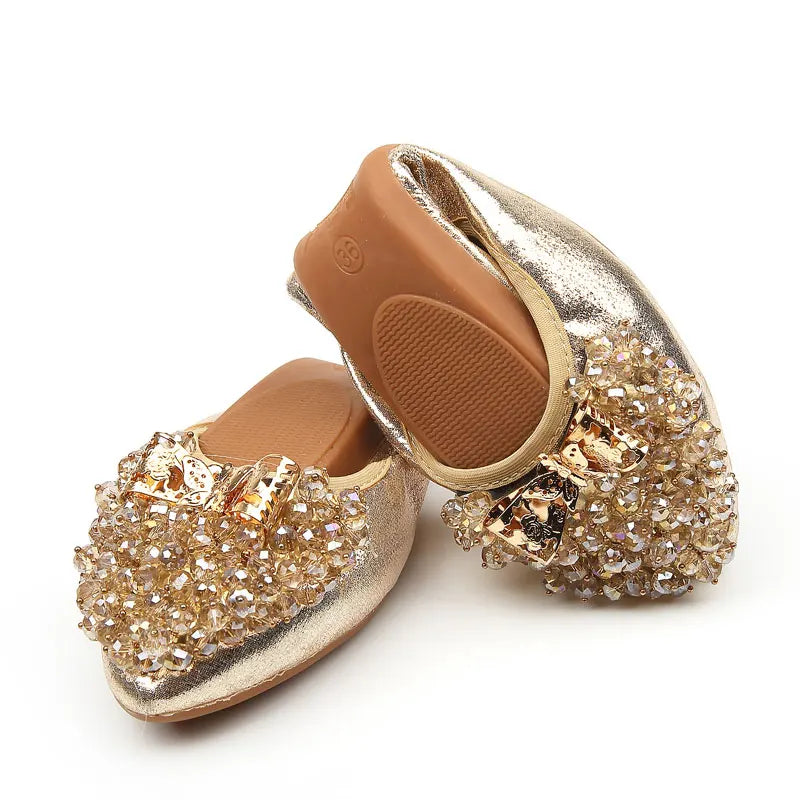 Folded gold ballet flat highlighting its flexible rubber sole and sparkling beaded toe cap.