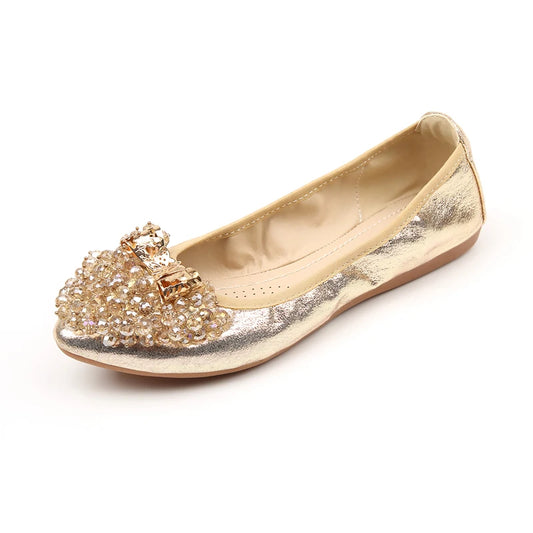 Foldable gold ballet flat with round toe, clustered crystal beads, metallic bow, and flat outsole (side profile).