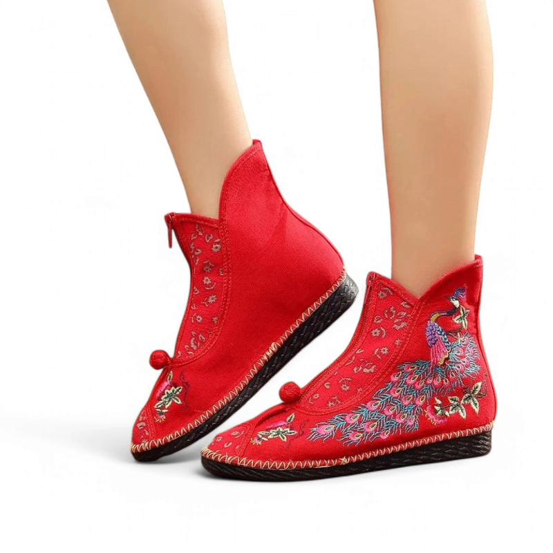 Red cotton ankle boot with peacock embroidery and front zipper, side-angled on foot.
