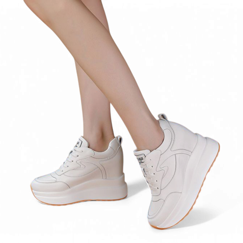 White wedge sneaker on crossed legs, showing platform height and caramel outsole.