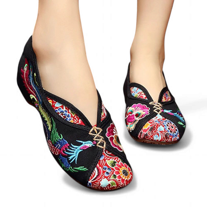 Front angle view of black embroidered canvas Mary Jane flats with V-throat vamp and knot strap, worn.