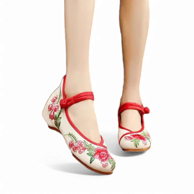 Front angle view of ivory canvas Mary Jane flats with red piping, floral embroidery, and a fabric knot strap.