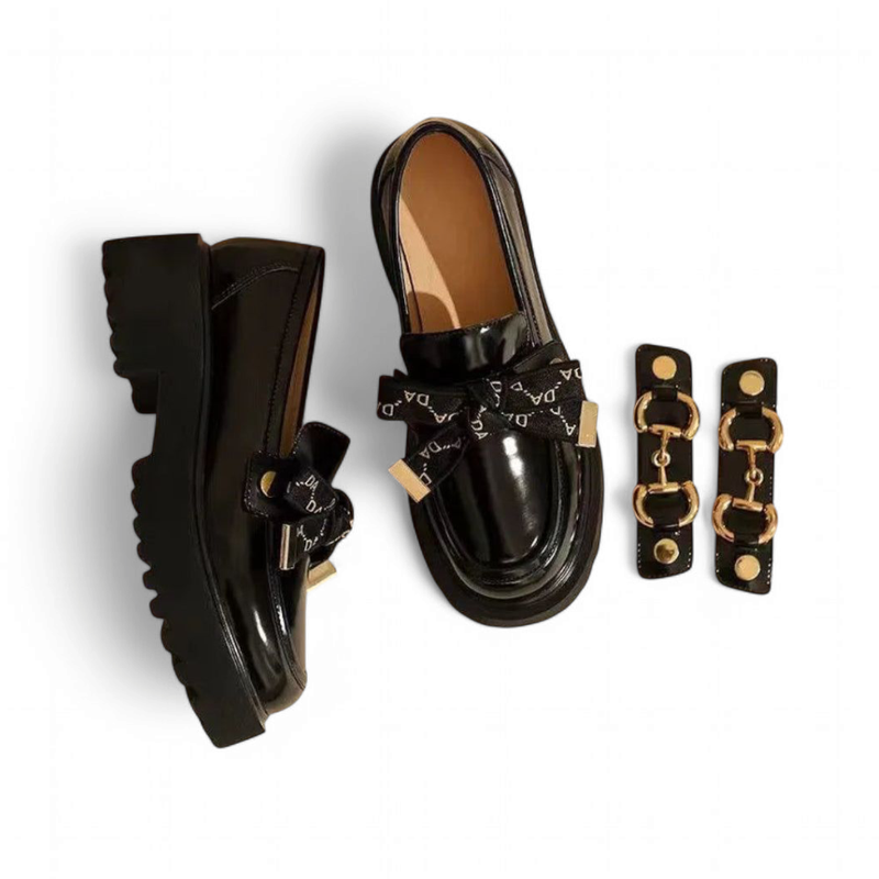 Glossy black loafer beside a detachable logo ribbon and gold horse-bit set.