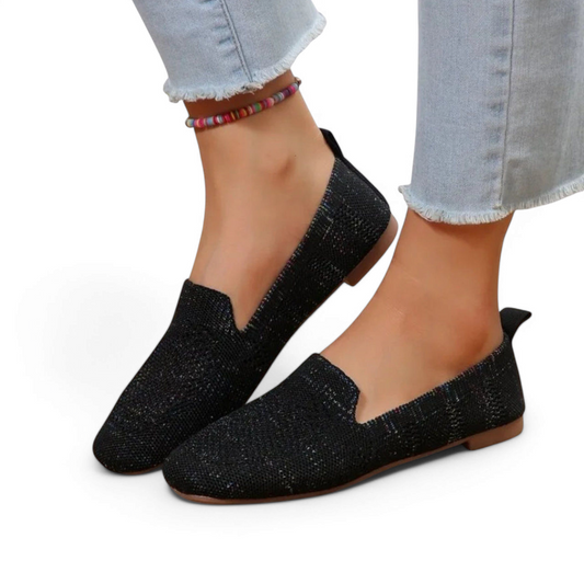On-foot three-quarter view of black knit loafers with flat rubber soles.