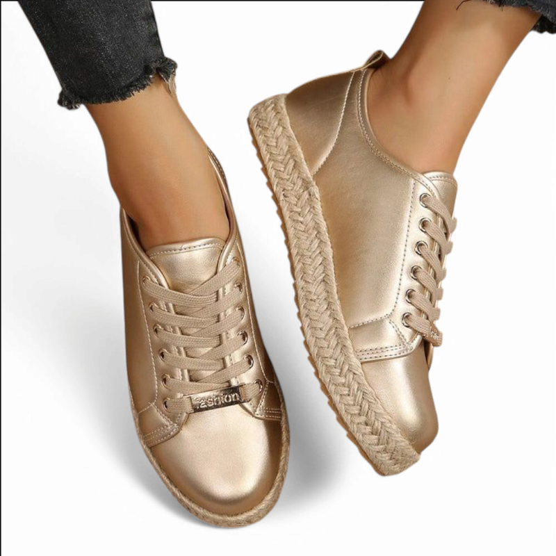 Pair of gold sneakers; one foot lifted to reveal the braided jute platform and metallic upper sheen.

