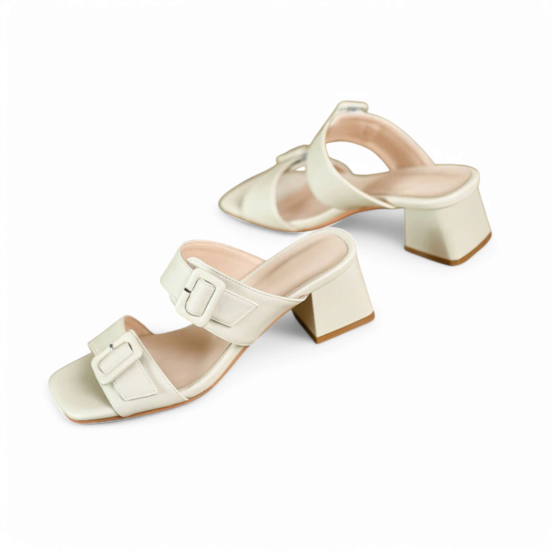 Cream slide sandals with mid block heels and twin buckle straps on a white backdrop.