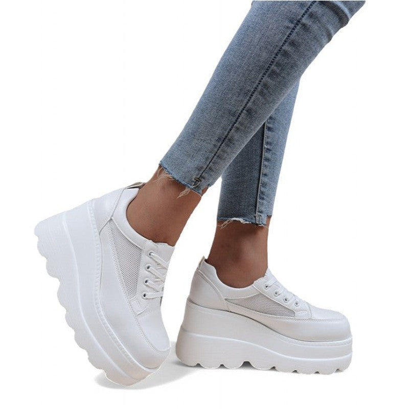 White round-toe wedge sneaker with high platform, worn with skinny jeans in side profile.