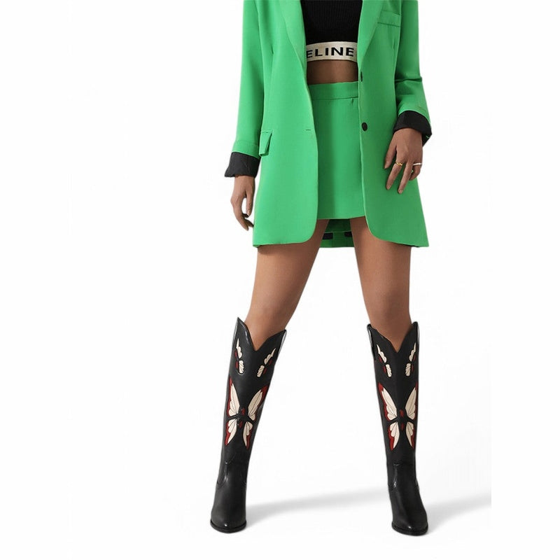 Full front view of black boots with red butterflies beneath a green suit.

