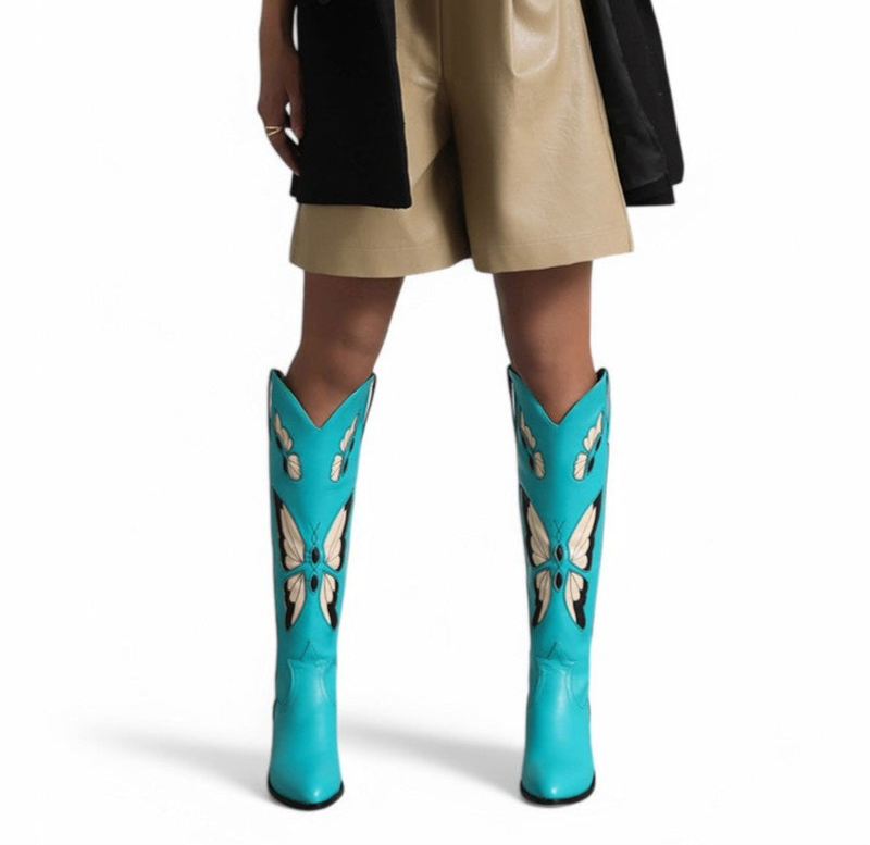 Front shot of knee-high turquoise boot with cream and black butterflies, worn by model.