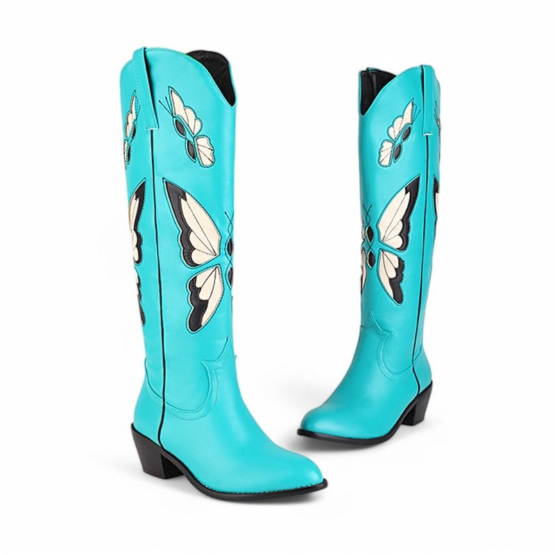 Studio pair of turquoise knee-high boots with cream butterflies and black outline on white background.

