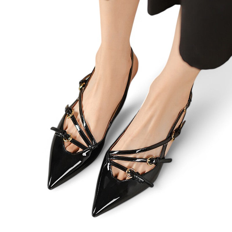 Black patent slingback pumps on feet, pointed toes crossing straps with gold buckles.
