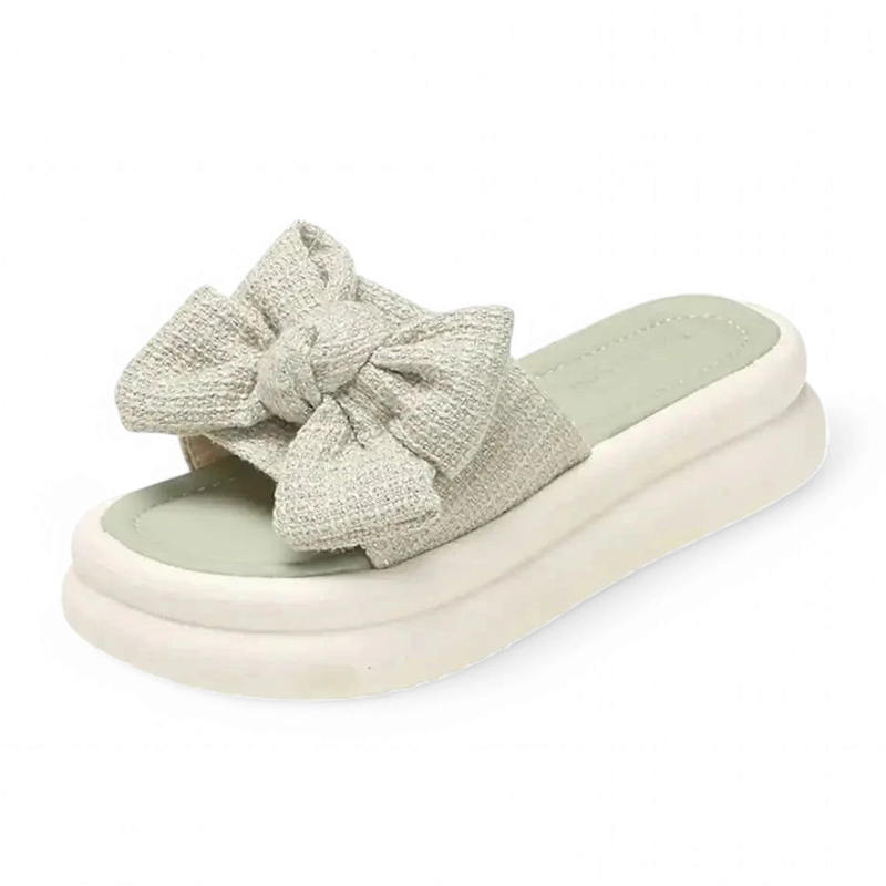 Sage-green slide sandal with an oversized fabric bow and low white platform sole.