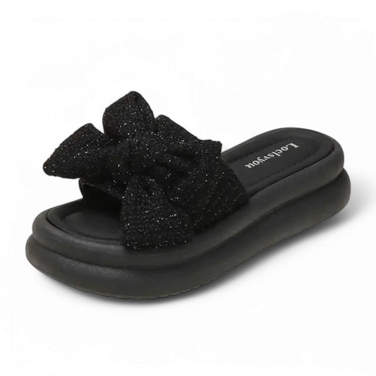 Black slide on a matching sole, topped with a subtly glittering fabric bow.