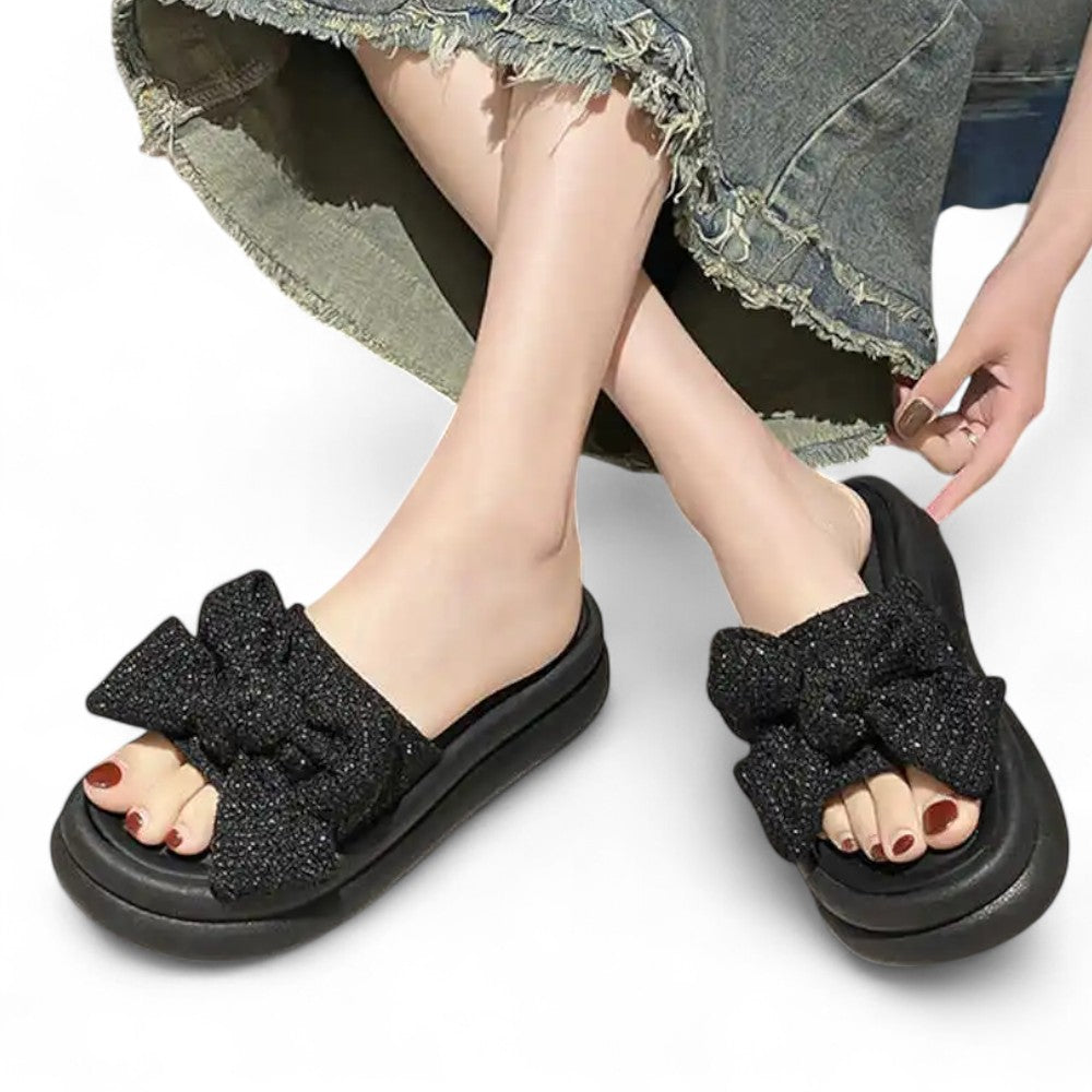 Black sandals with bow details worn by a model on a white background
