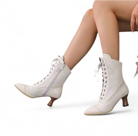 White mid-calf boot with front lacing and side zipper, pointed-almond cap toe with brogue trim, curved 5 cm kitten heel, shown in on-foot side view.