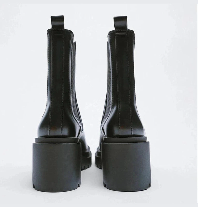 A pair of black boots viewed from the back, highlighting the high chunky heels and straight stitched lines.