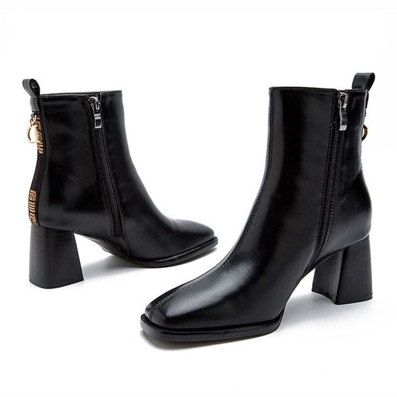 Pair of black leather ankle boots with mid block heel and side zipper on white background.

