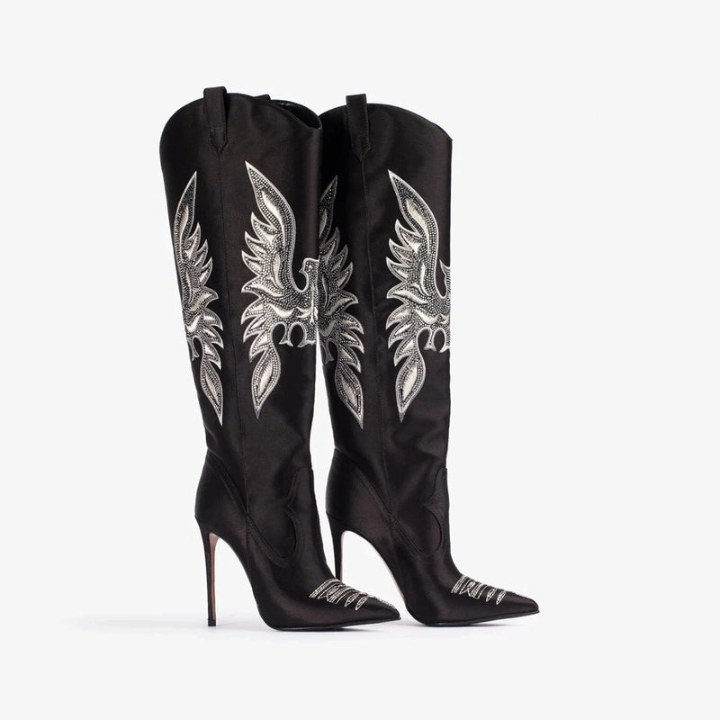 Tall black boots with bold bird embroidery, shown from the side with thin high heels and pointed toes.
