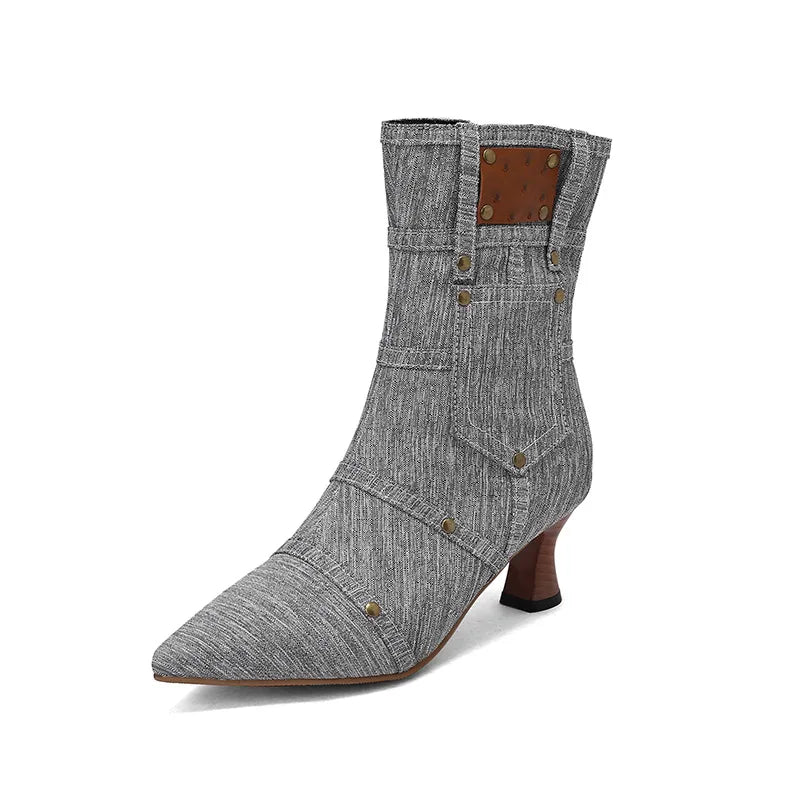 Grey denim ankle boot with rivets, pointed toe and kitten heel on white background.