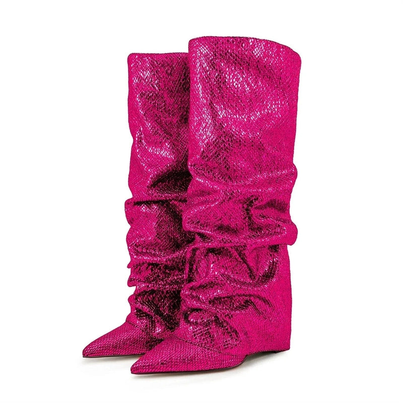 Pair of pink knee-high boots shown from an angled front-side view, with pointed toes, slouchy jeweled shafts, and hidden wedge heels, set against a white background.