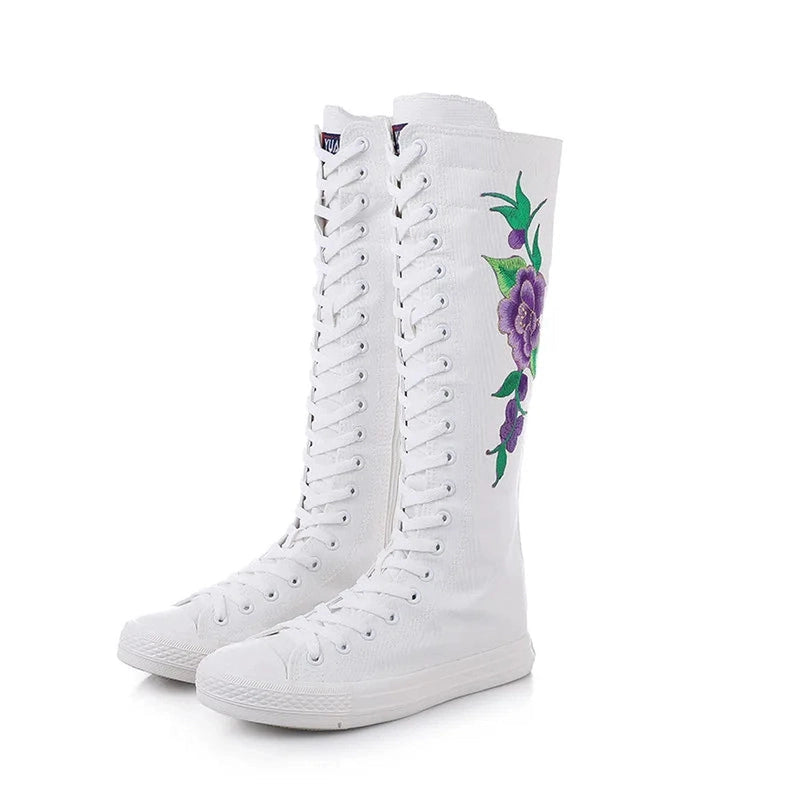 Partial front view of white lace-up boots with hidden zipper and purple embroidery.
