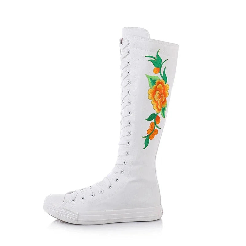 Side view of white knee-high canvas boot showing orange flower and green leaves embroidery.
