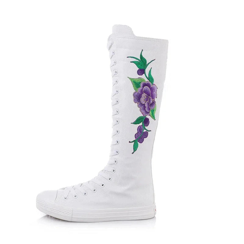 Side view of knee-high white canvas boot with full lacing and purple-green floral embroidery.
