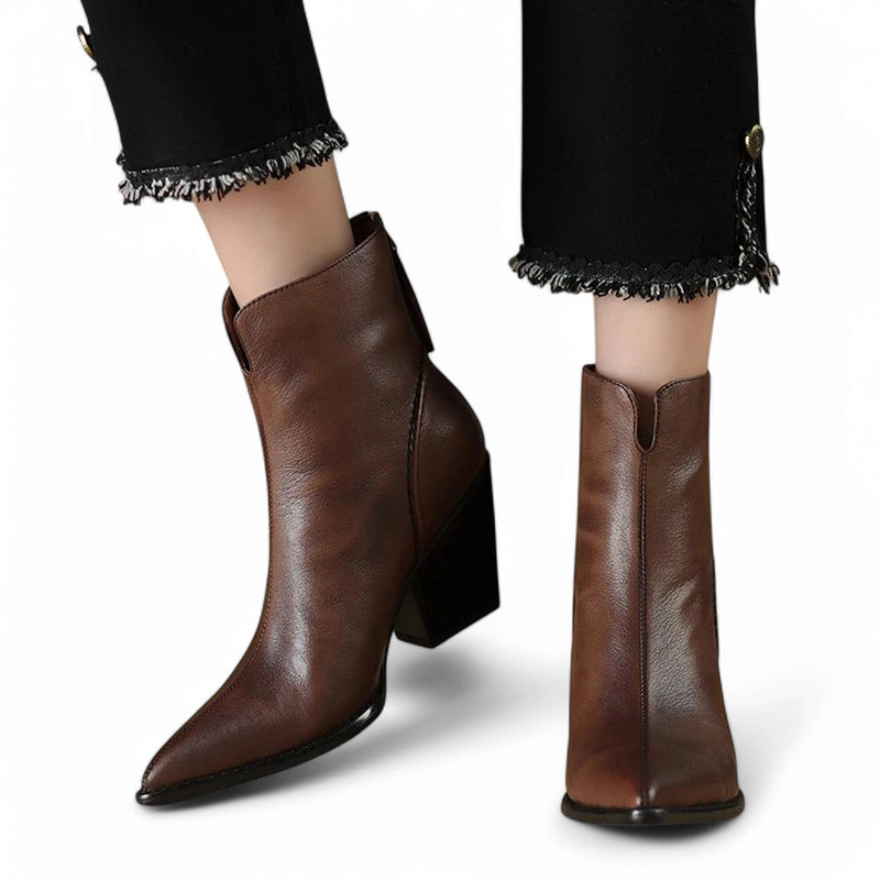 Pair of brown pointed leather boots with high heels, shown worn with fringed black pants.

