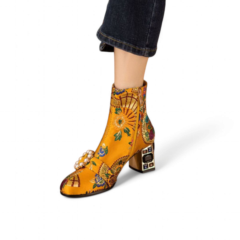 Yellow floral-brocade ankle boot with pearl buckle and gem-set heel, shown on a model in cropped jeans.