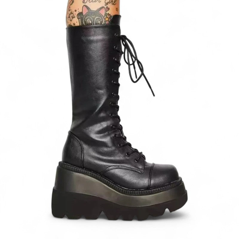 Side profile of tall black lace‑up platform boot on tattooed leg.